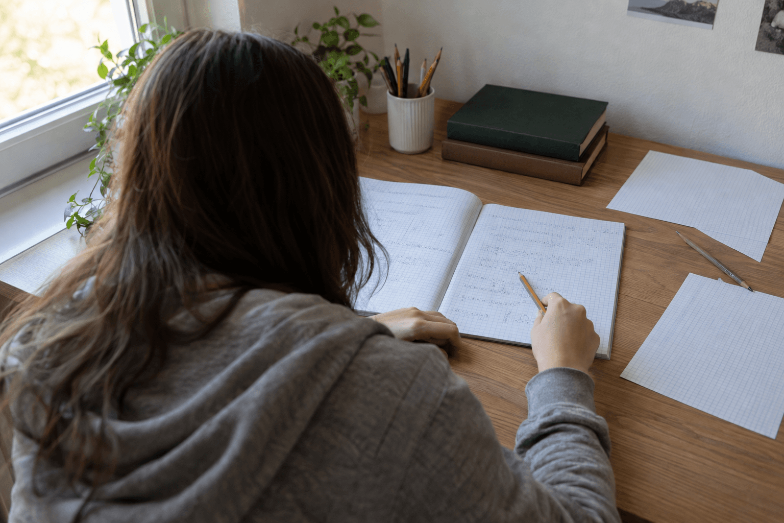 Elevă văzută din spate, comparând două pagini cu exerciții de matematică la un birou