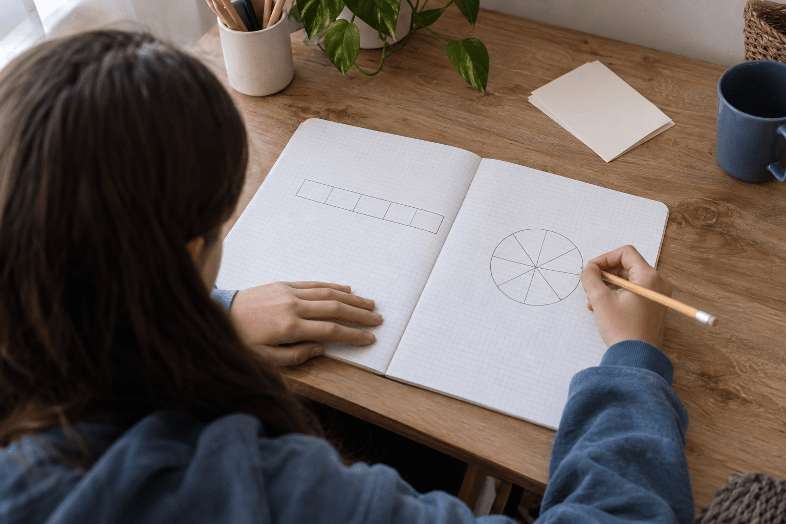 Elevă văzută de sus și din spate, desenând o bară procentuală și un cerc împărțit în caiet