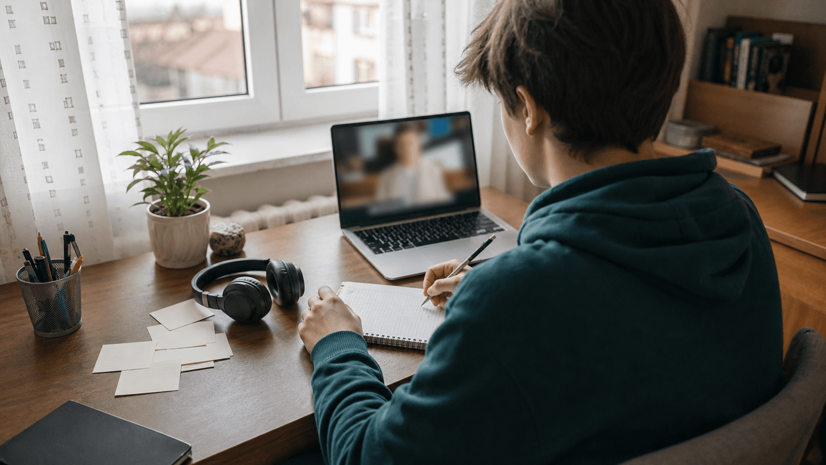 Elev care învață engleză singur la un birou de acasă, cu laptop, căști și caiet